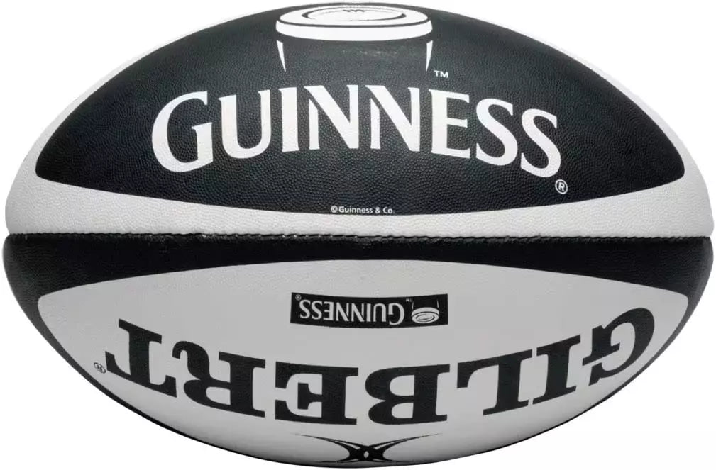 The Guinness X Gilbert Rugby Ball, prominently displaying the names "Guinness" and "Gilbert," is showcased upside down in black and white, highlighting its distinct branding from the Guinness Webstore UK.