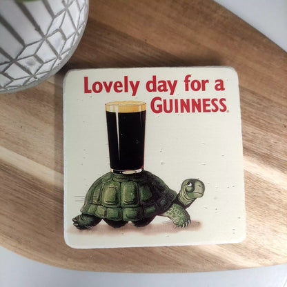 The Guinness Stone Effect Coaster - Gilroy Tortoise from the Guinness Webstore UK features a delightful design of a turtle carrying a pint of Guinness and the caption "Lovely day for a Guinness." It's an essential addition for any true fan of Guinness.