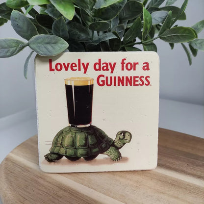 The Guinness Stone Effect Coaster from the Guinness Webstore UK showcases the iconic Gilroy Tortoise balancing a pint of Guinness on its shell alongside a touch of nature in the background, making it an enchanting home accessory.