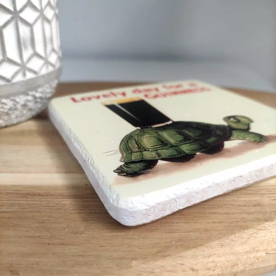 This delightful home accessory, the Guinness Stone Effect Coaster - Gilroy Tortoise from Guinness Webstore UK, showcases a ceramic coaster resting on a wooden base, adorned with an illustration of the Gilroy Tortoise carrying a stack of books. It’s perfect for adding character to any room and is as unique and charming as a collection of Guinness coasters.