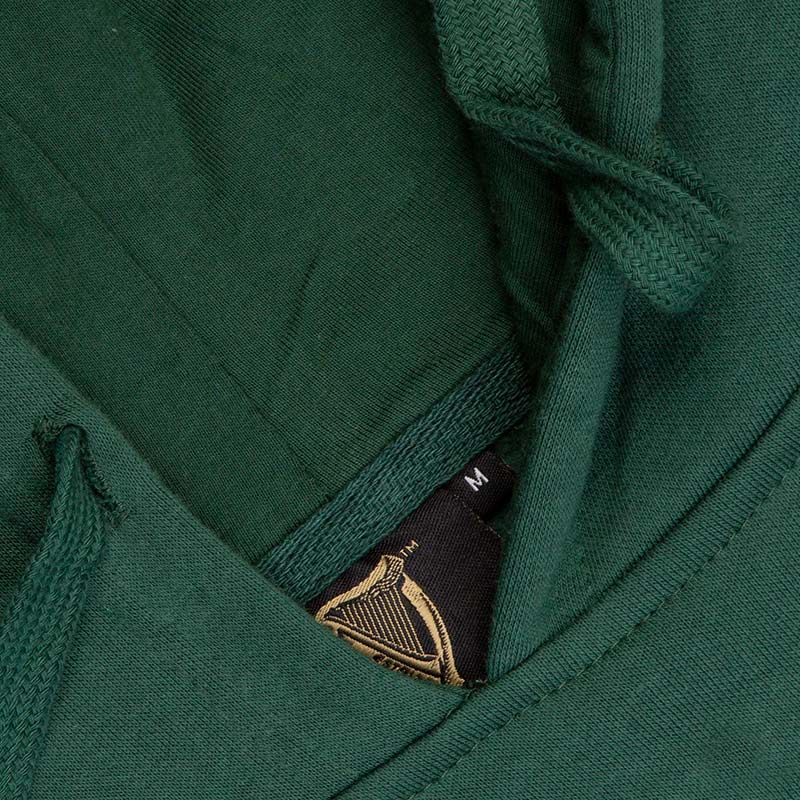 Close-up of a Guinness Bottle Green Unisex Hoodie with a label showing size m and a gold crown logo on the tag.